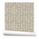 Partially unrolled wallpaper in a repeating curvolinear print in navy on a painted tan field.