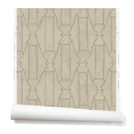Partially unrolled wallpaper in a repeating curvolinear print in gold on a painted cream field.