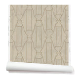 Partially unrolled wallpaper in a repeating curvolinear print in gold on a painted cream field.