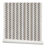 Partially unrolled wallpaper in a repeating mosaic stripe print in shades of blue, rust and gray on a cream field.