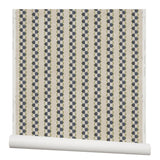 Partially unrolled wallpaper in a repeating mosaic stripe print in shades of green and gray-blue on a tan field.