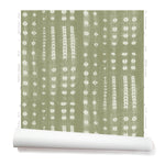 A partially unrolled roll of wallpaper in a striped print inspired by Japanese shibori on a sage green background.