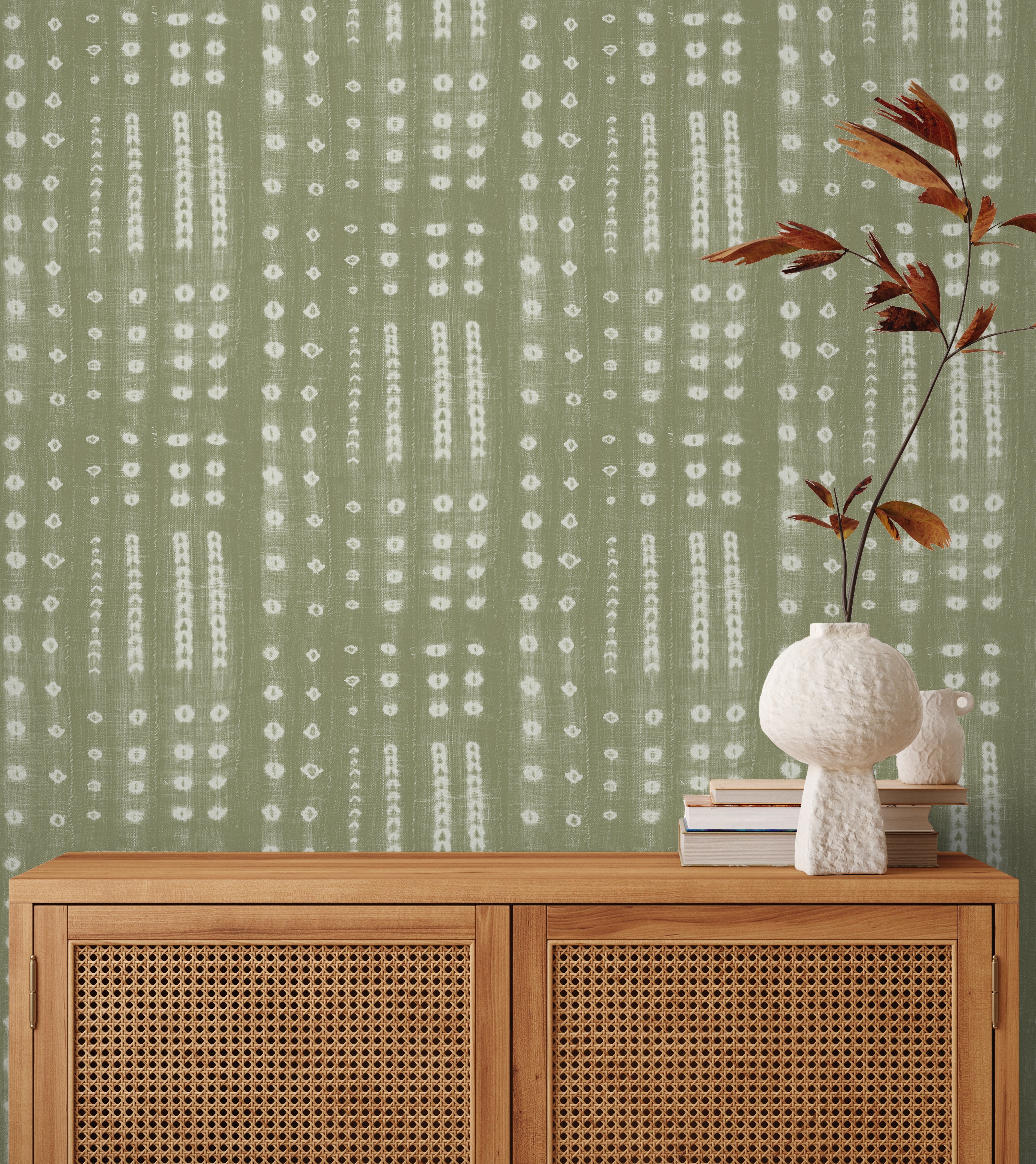 A wooden credenza with a vase and bookes in front of wallpaper in a striped print inspired by Japanese shibori on a sage green background.
