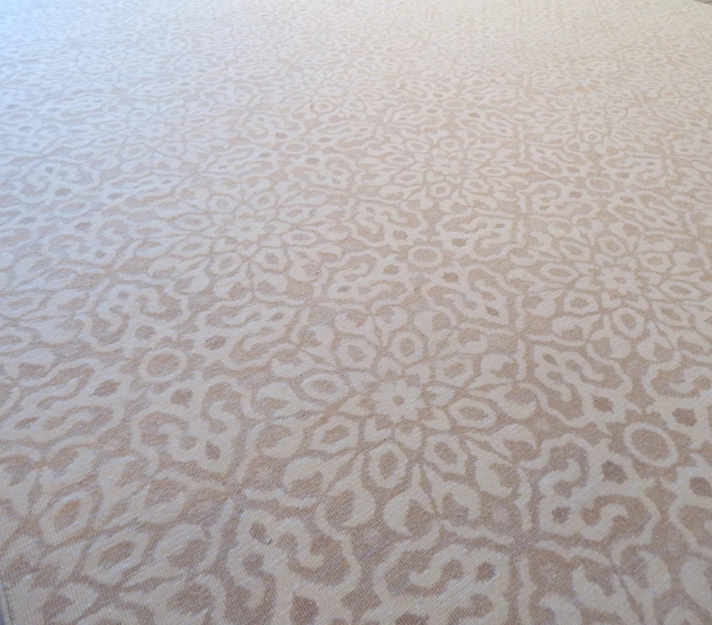 A close-up of a light beige and off-white patterned carpet with an intricate repeating damask medallion design.