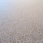 A close-up of a light beige and off-white patterned carpet with an intricate repeating damask medallion design.