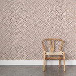 A wooden chair stands in front of a wall papered in a painterly animal print in cream and brown on a dusty pink field.