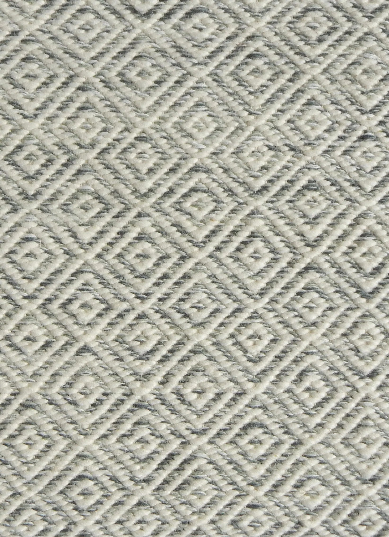 Detail of handwoven rug with diamond pattern in cream and shades of grey-blue.