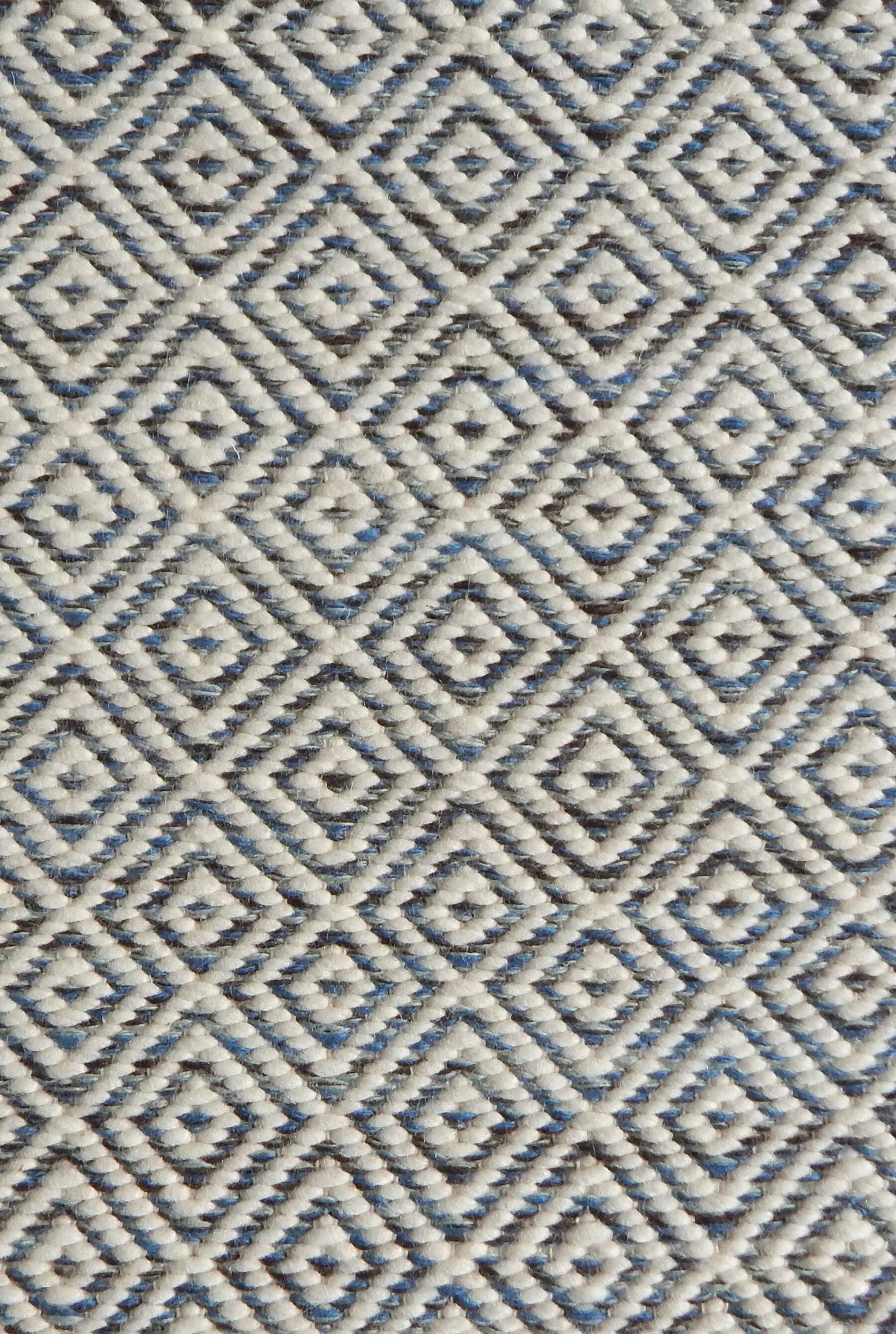 Detail of handwoven rug with diamond pattern in cream and shades of blue and brown.