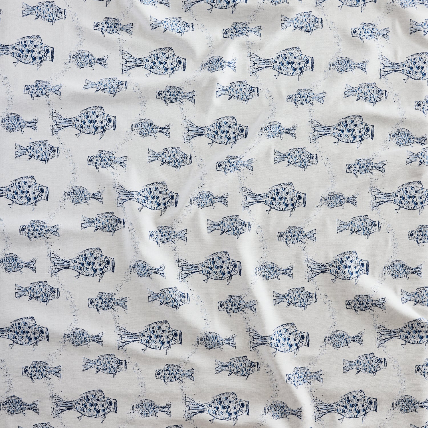 Close up of gently draped woven Indoor-Outdoor fabric with playful fish print in shades of blue on white. 