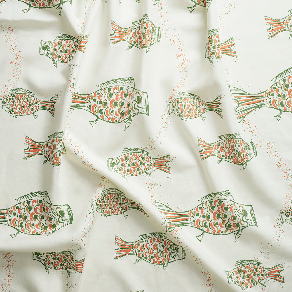 Close up of gently draped printed linen with a pattern of hand-drawn fish in green with tan and orange scales and scattered black bubble dots on white background.
