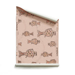 Roll of wallpaper with a pattern of hand-drawn fish in black with tan and pink scales and scattered black bubble dots on light pink. 