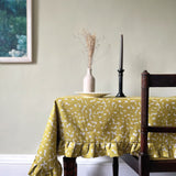A cozy dining room tableau with a wooden table topped in a ruffled polka dot tablecloth in mustard and white.