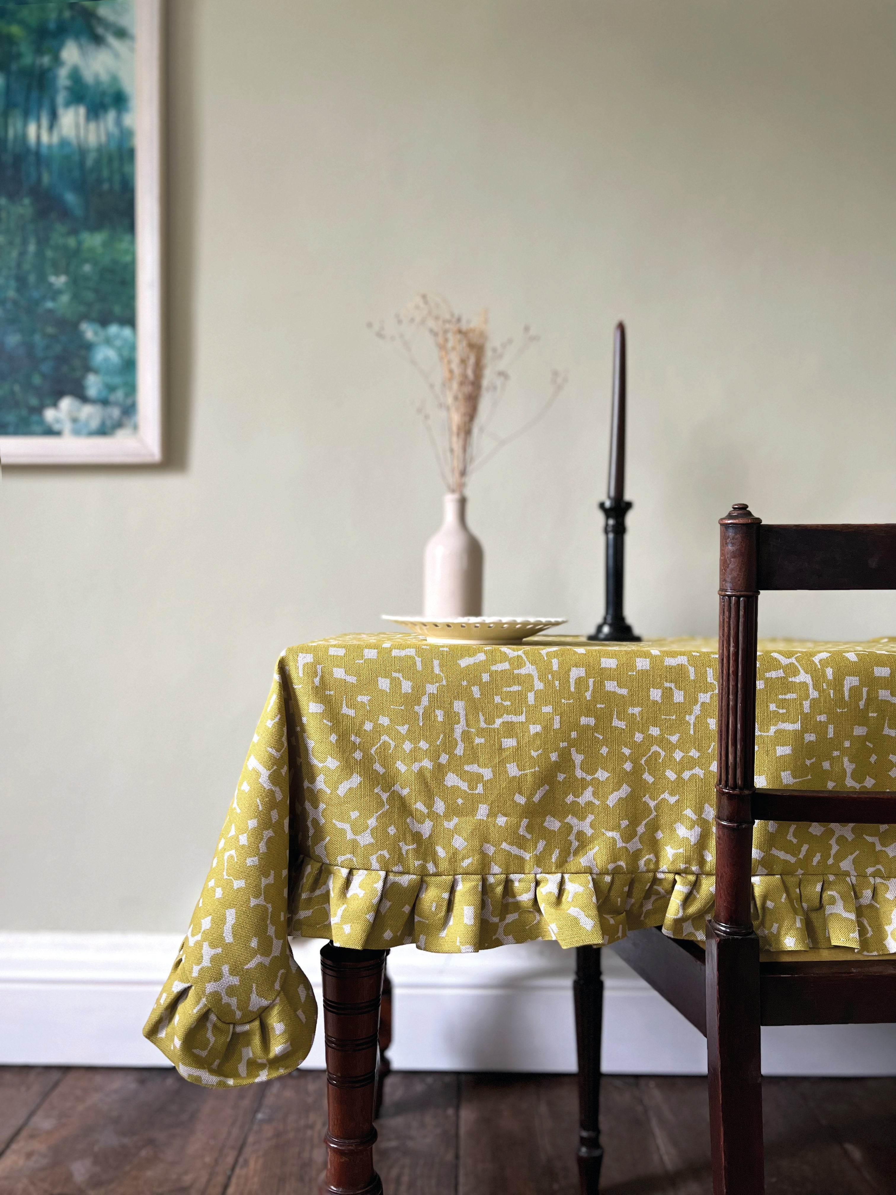 A cozy dining room tableau with a wooden table topped in a ruffled polka dot tablecloth in mustard and white.