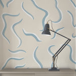 A desk lamp stands in front of a wall papered in a painterly botanical print in blue, white and tan.