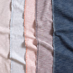 Gently draped fabric with textural weave and selvedge edge in white, light blue, coral pink, blue and navy blue. 