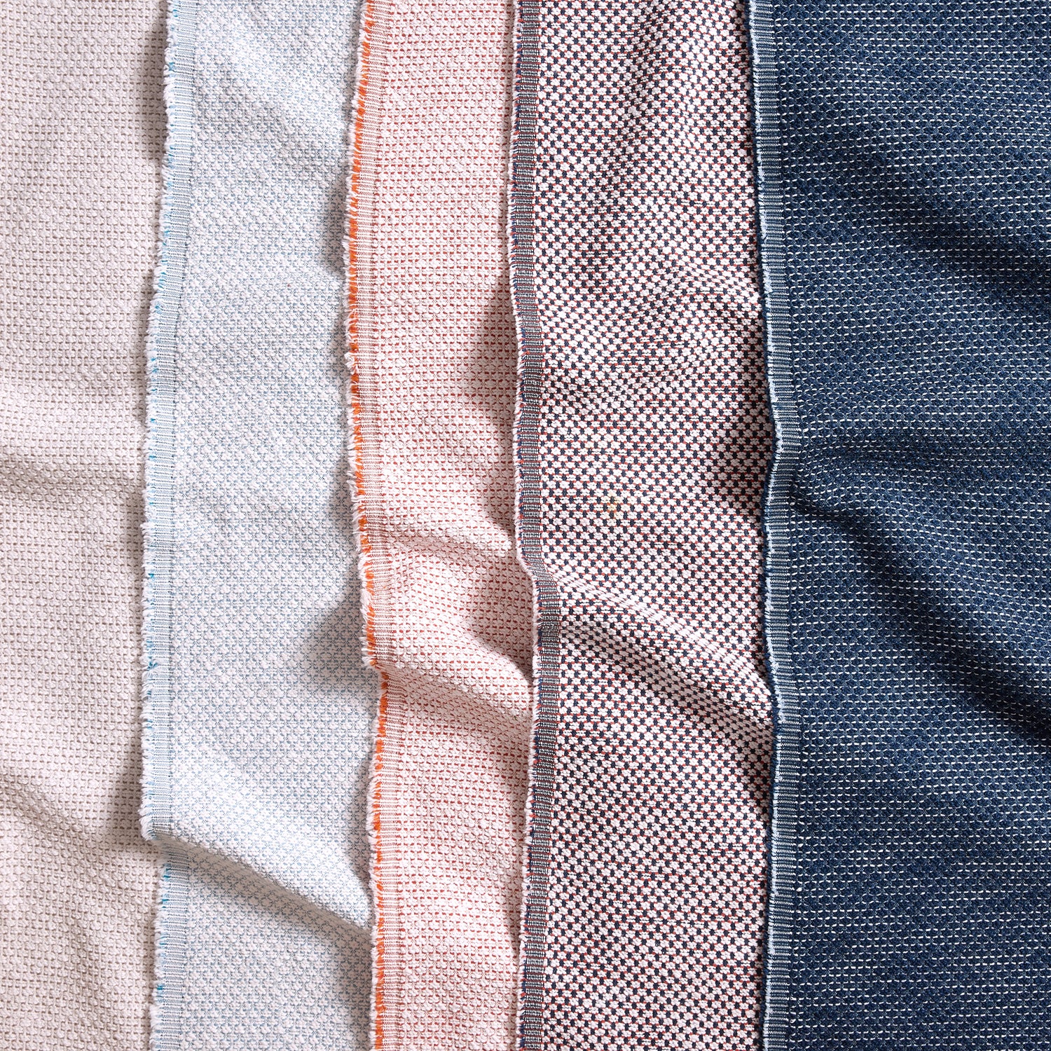 Gently draped fabric with textural weave and selvedge edge in white, light blue, coral pink, blue and navy blue. 