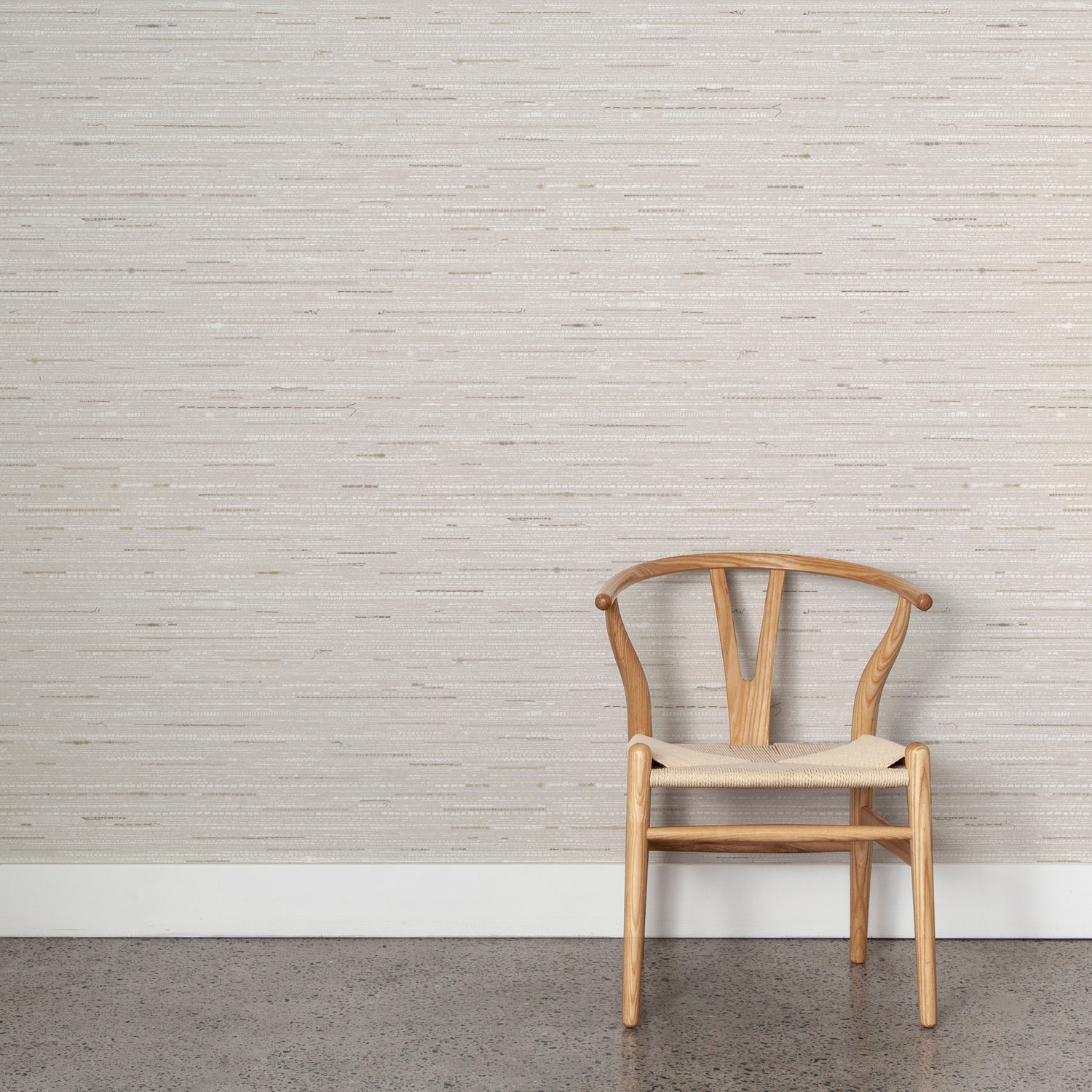 Wooden chair with woven seat on concrete floor against wallpaper in a textural striped pattern in shades of beige and grey.