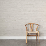 Wooden chair with woven seat on concrete floor against wallpaper in a textural striped pattern in shades of beige and grey.