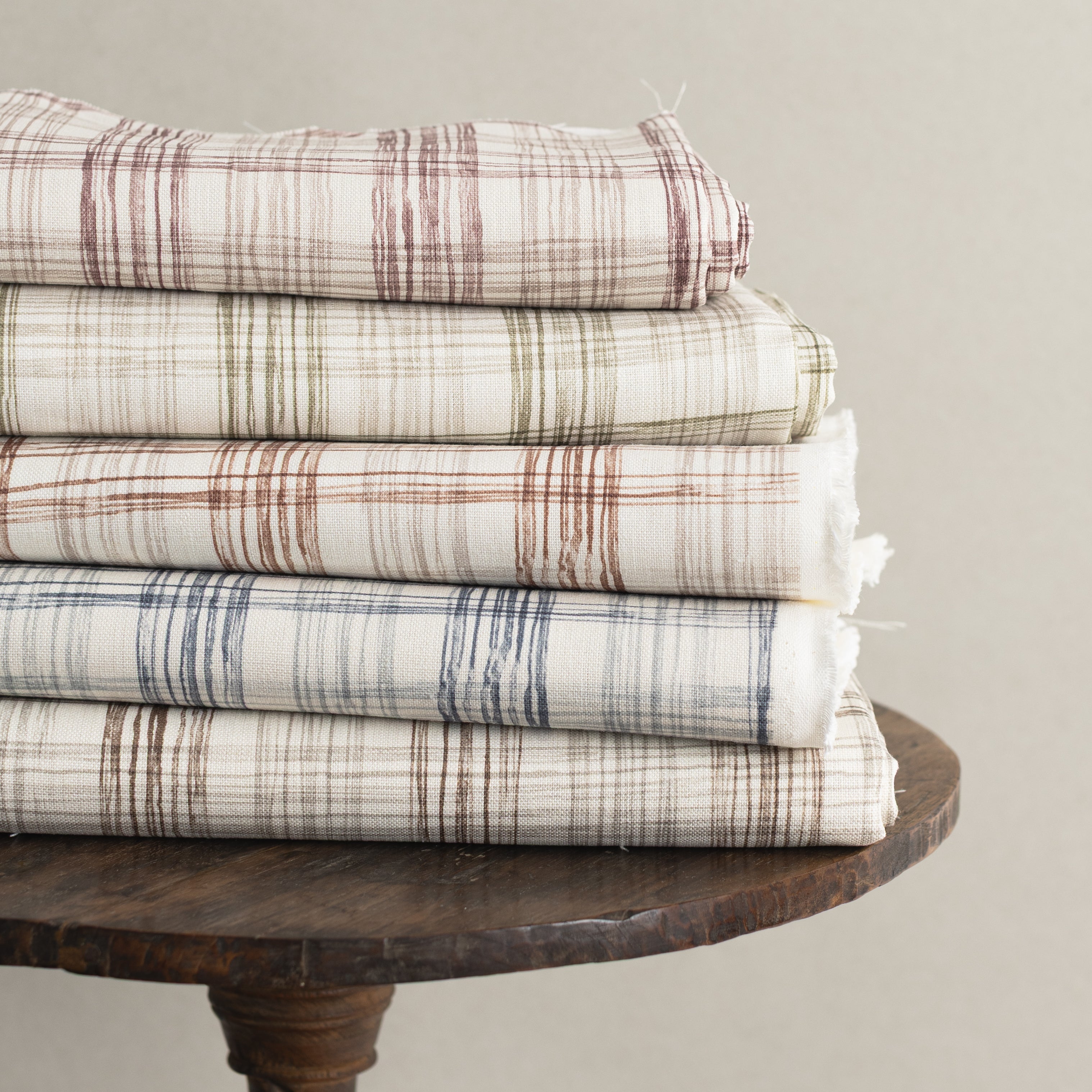 Stack of plaid fabrics on a wooden table against a neutral background