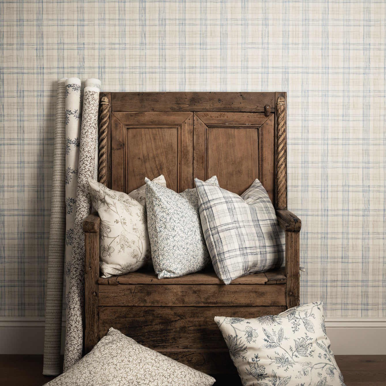 Wooden bench with patterned cushions against a plaid wallpapered wall.