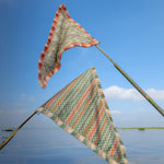 Two colorful triangular flags on a stick over a body of water with a clear blue sky.