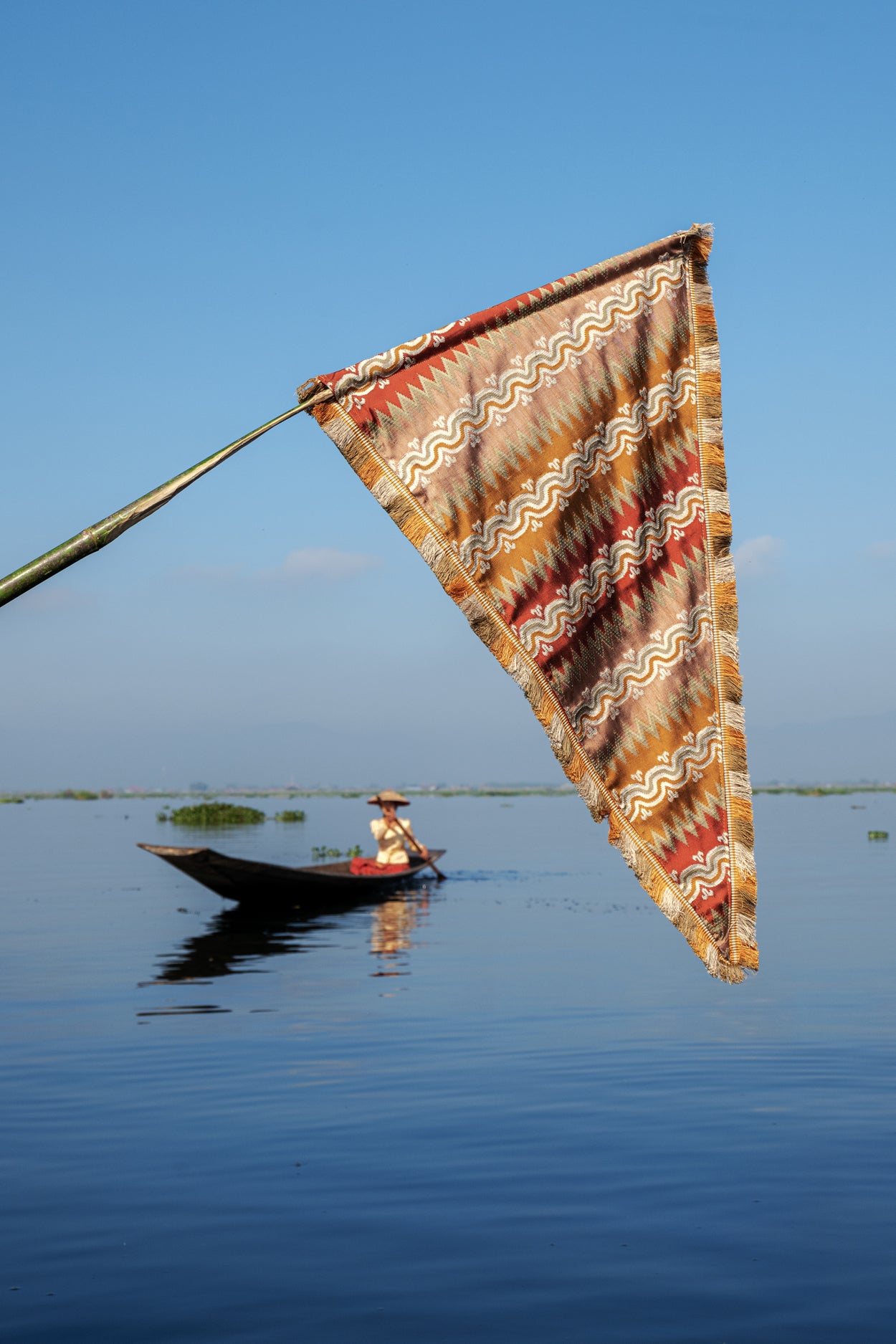 Traditional boat with a colorful flag in the foreground on a calm body of water under a clear blue sky.