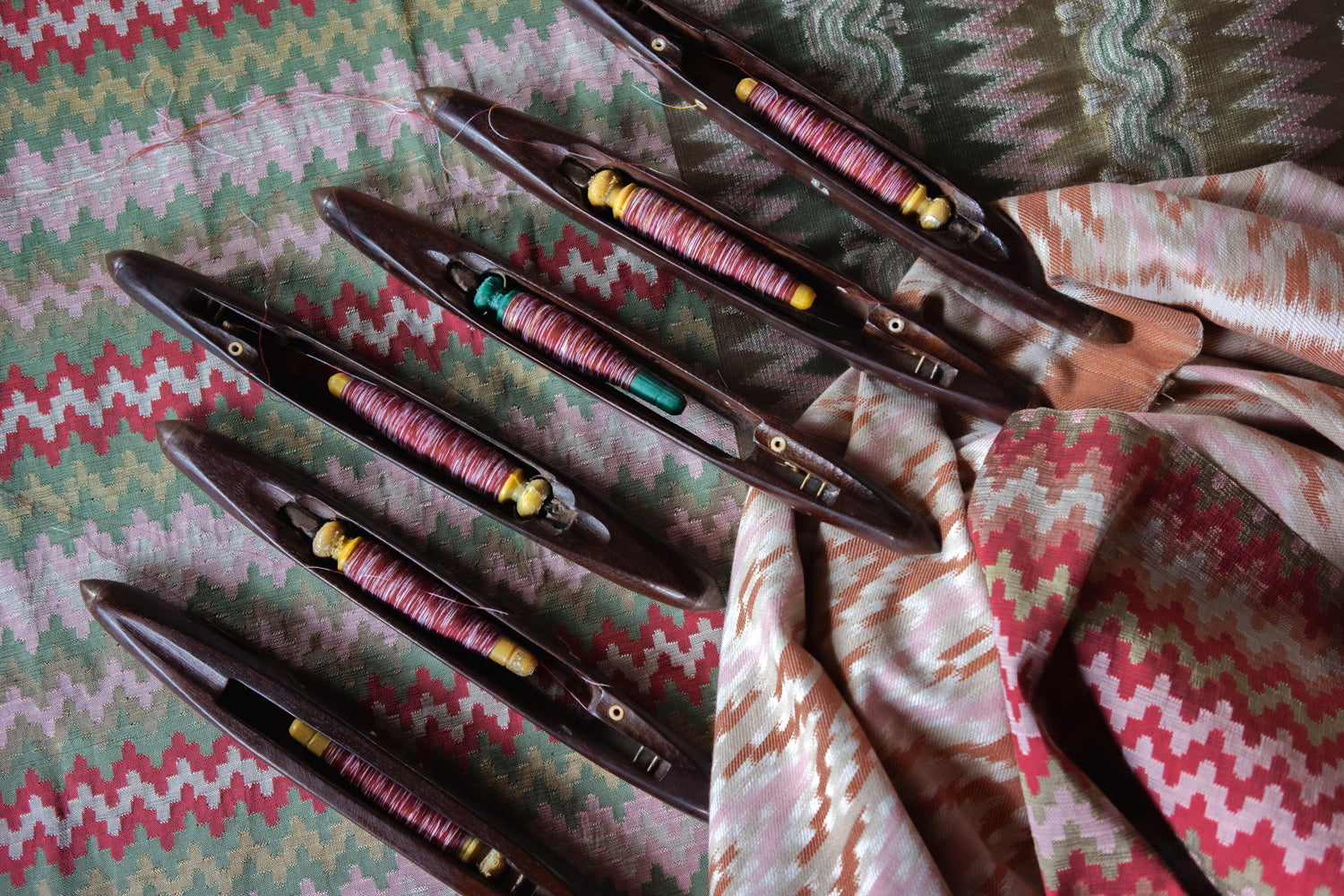 Set of wooden shuttles with colorful thread on a patterned fabric background