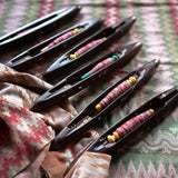 Set of black weaving shuttles with colorful thread on a patterned fabric background