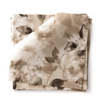 Stacked swatches of fabric in a painterly leaf print in shades of warm brown on a white background.