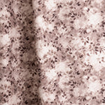 Gently draped fabric in a painterly leaf print in shades of wine purple and mauve with a mottled white overlay.