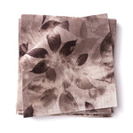 Stacked swatches of fabric in a painterly leaf print in shades of muted purple on a white background.
