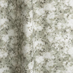 Gently draped fabric in a painterly leaf print in shades of grey-green with a mottled white overlay.