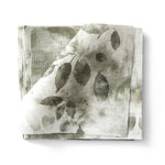 Stacked swatches of fabric in a painterly leaf print in shades of muted grey-green on a white background.