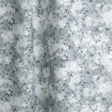 Gently draped fabric in a painterly leaf print in shades of steel blue and teal with a mottled white overlay.