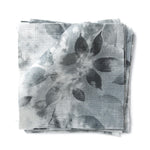 Stacked swatches of fabric in a painterly leaf print in shades of blue on a white background.