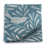 A stack of fabric swatches in a playful bird and leaf print in cream on a blue field.