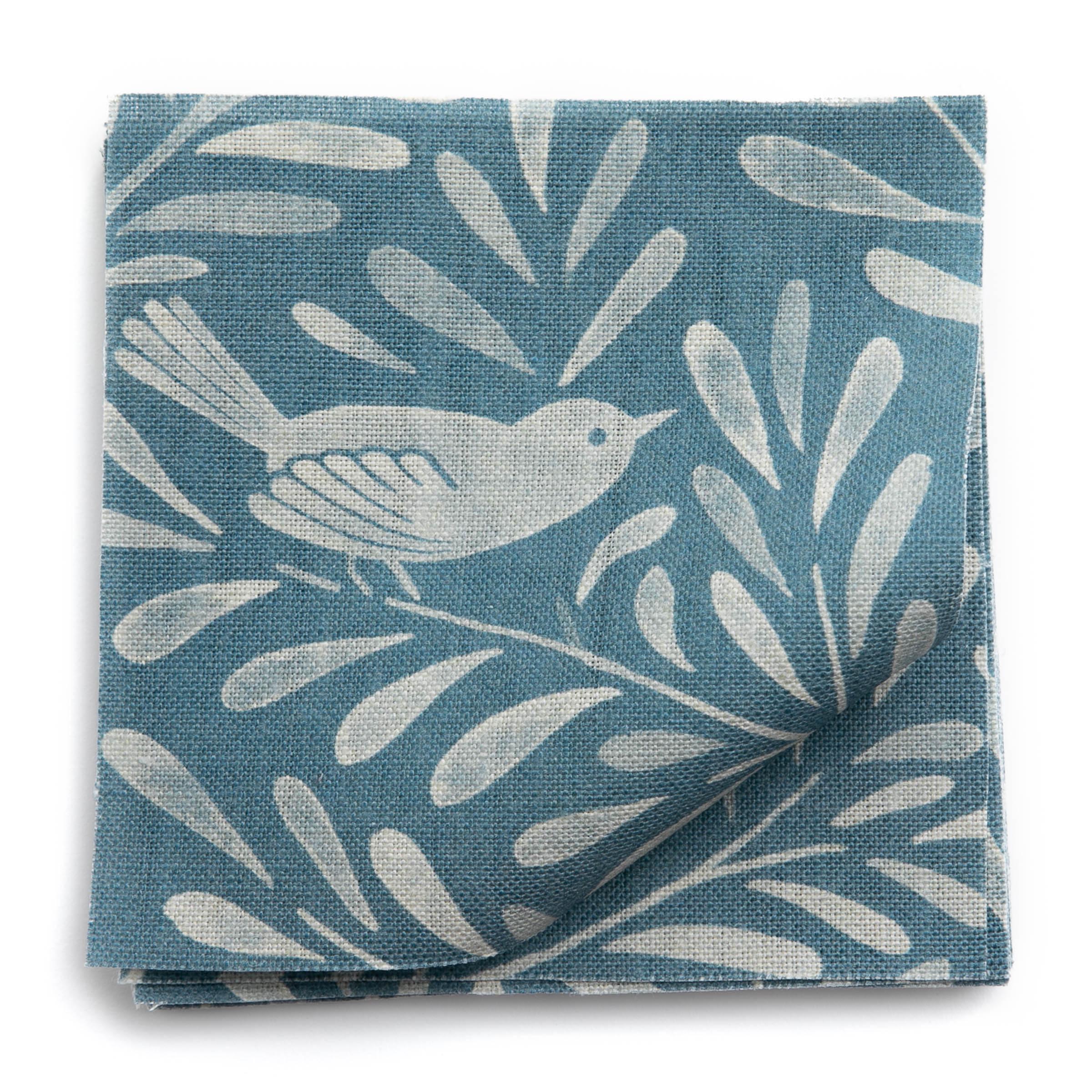 A stack of fabric swatches in a playful bird and leaf print in cream on a blue field.