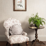 Decorative armchair with floral pattern, side table with plants, and framed artwork on striped wall.