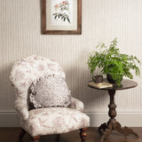 Decorative armchair with floral pattern, side table with plants, and framed artwork on striped wall.