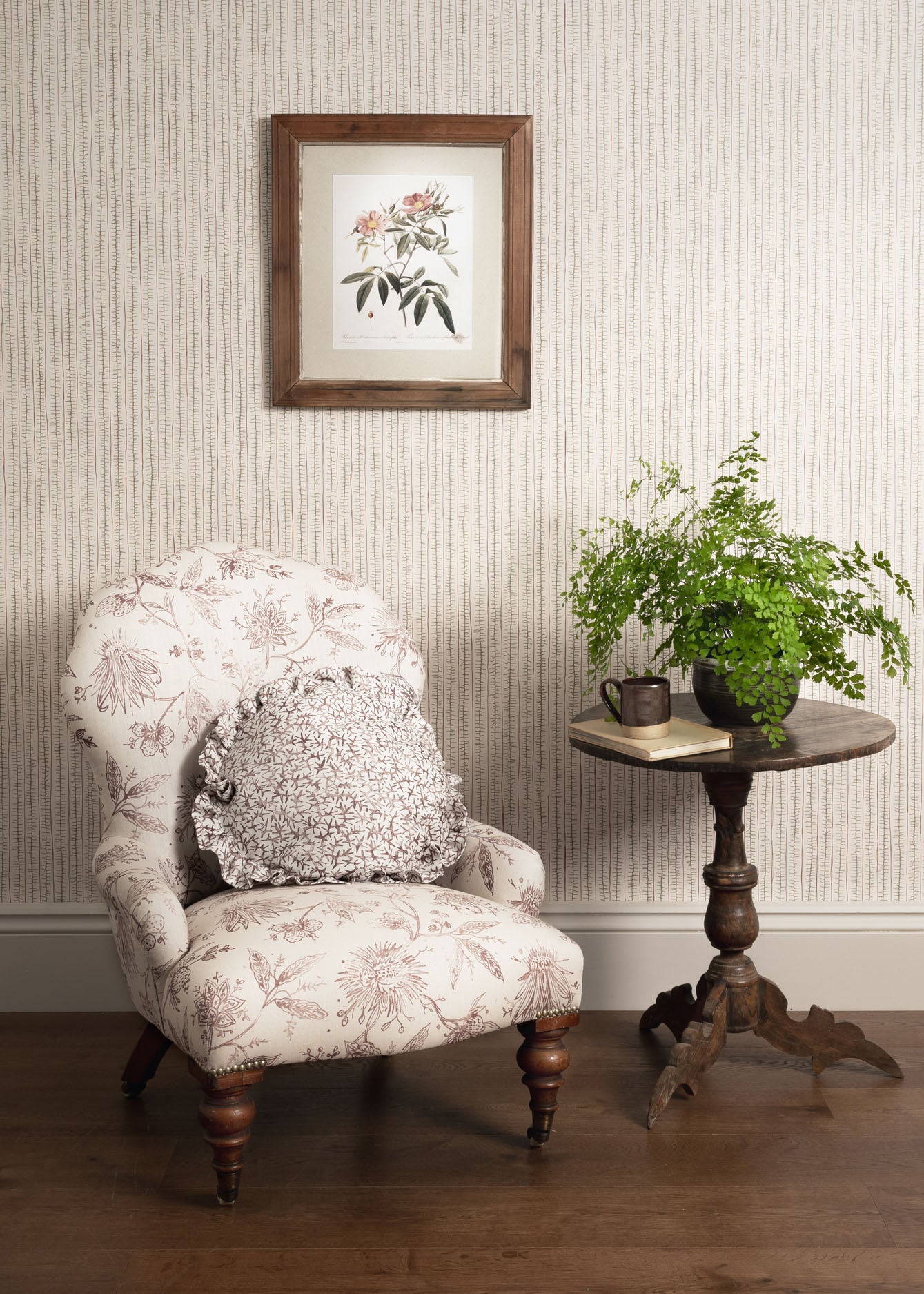 Decorative armchair with floral pattern, side table with plants, and framed artwork on striped wall.