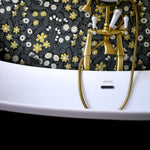 Detail shot of gilded bathtub faucets in front of a wall papered in a small-scale floral print in white, black and yellow.