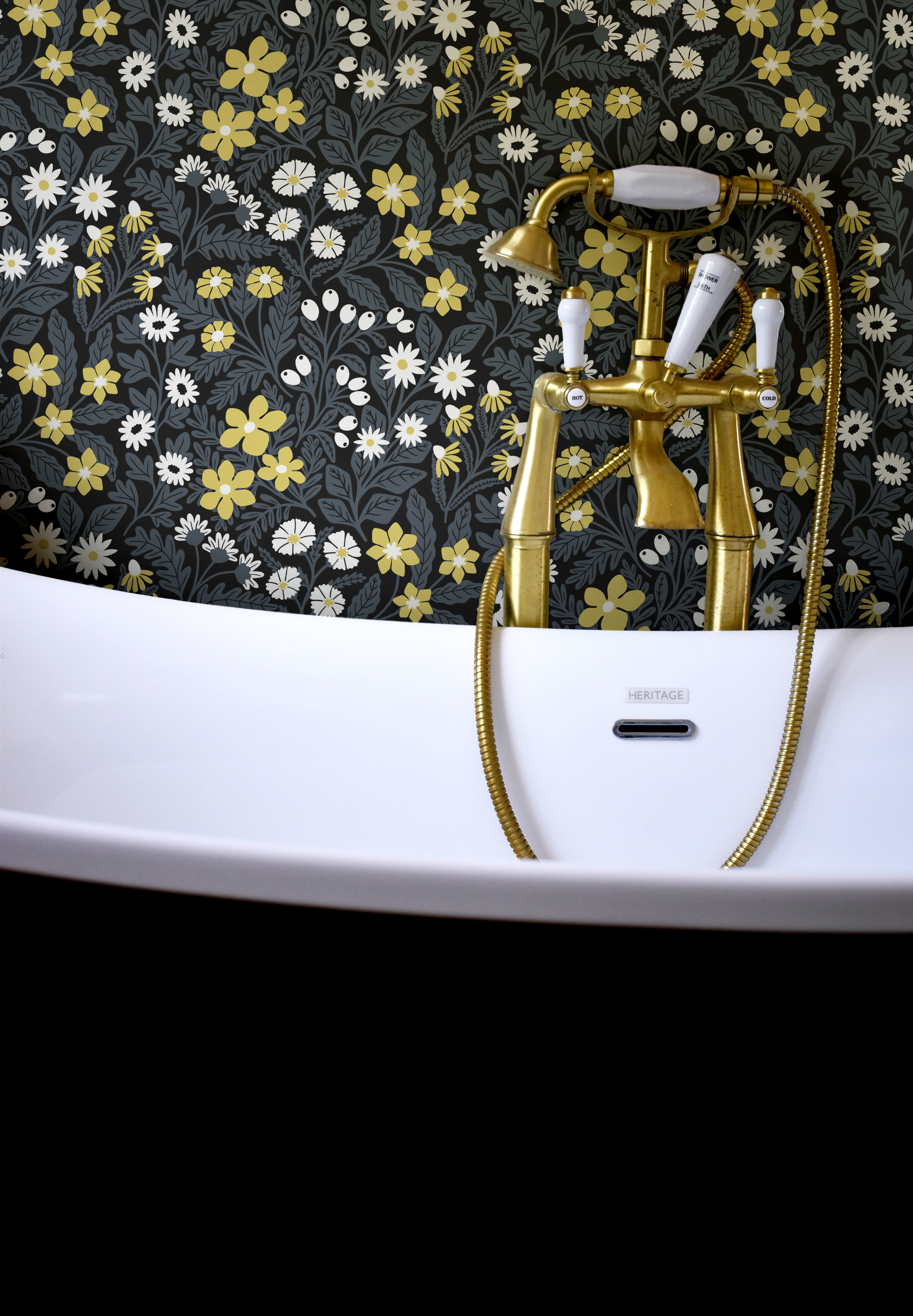 Detail shot of gilded bathtub faucets in front of a wall papered in a small-scale floral print in white, black and yellow.