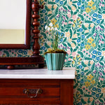 An end table with a potted plant stands in front of a wall papered in a multicolor small-scale floral print.