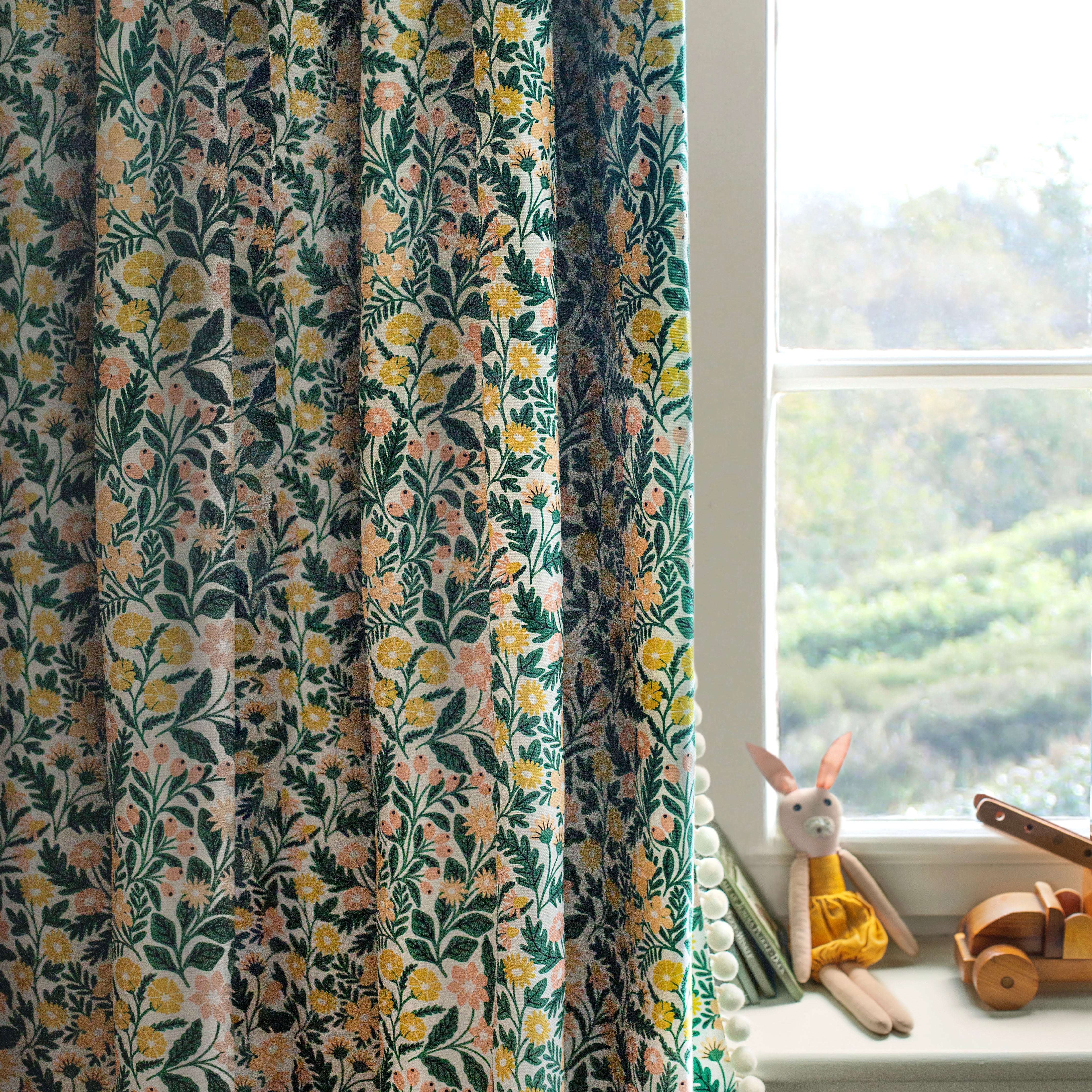 A children's room with a window and curtain in a small-scale floral print in green, yellow and coral on a white field.