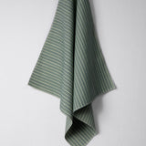 Draped woven outdoor fabric in a subtle stripe design in green and blue on a white wall. 