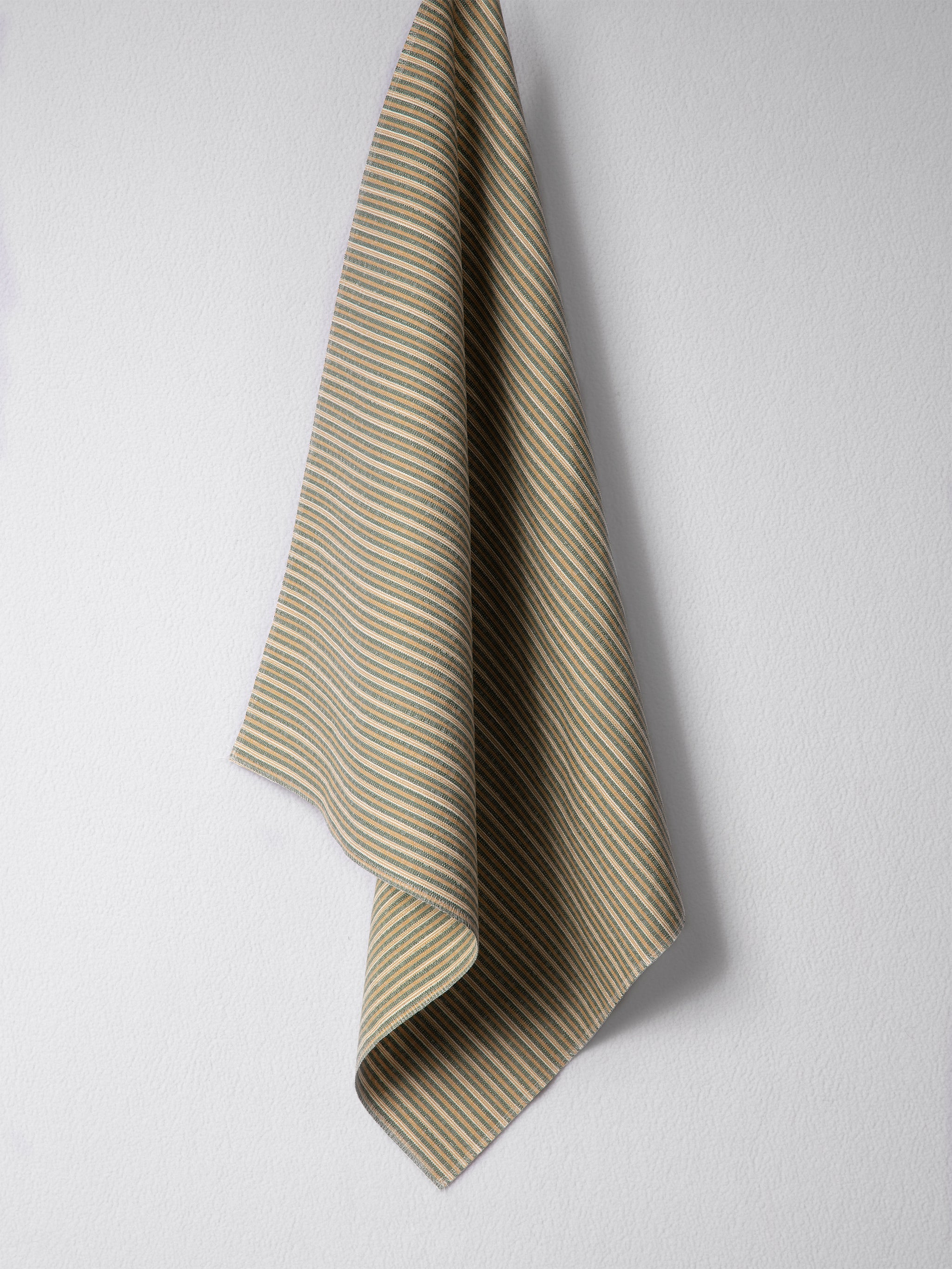 Draped woven outdoor fabric in a subtle stripe design in green and tan on a white wall. 