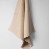 Draped woven outdoor fabric in a subtle stripe design in tan on a white wall. 