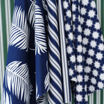 Hanging swatches of performance fabric in blue and white in a palm frond, stripe and moroccan star pattern on a green and white striped background.