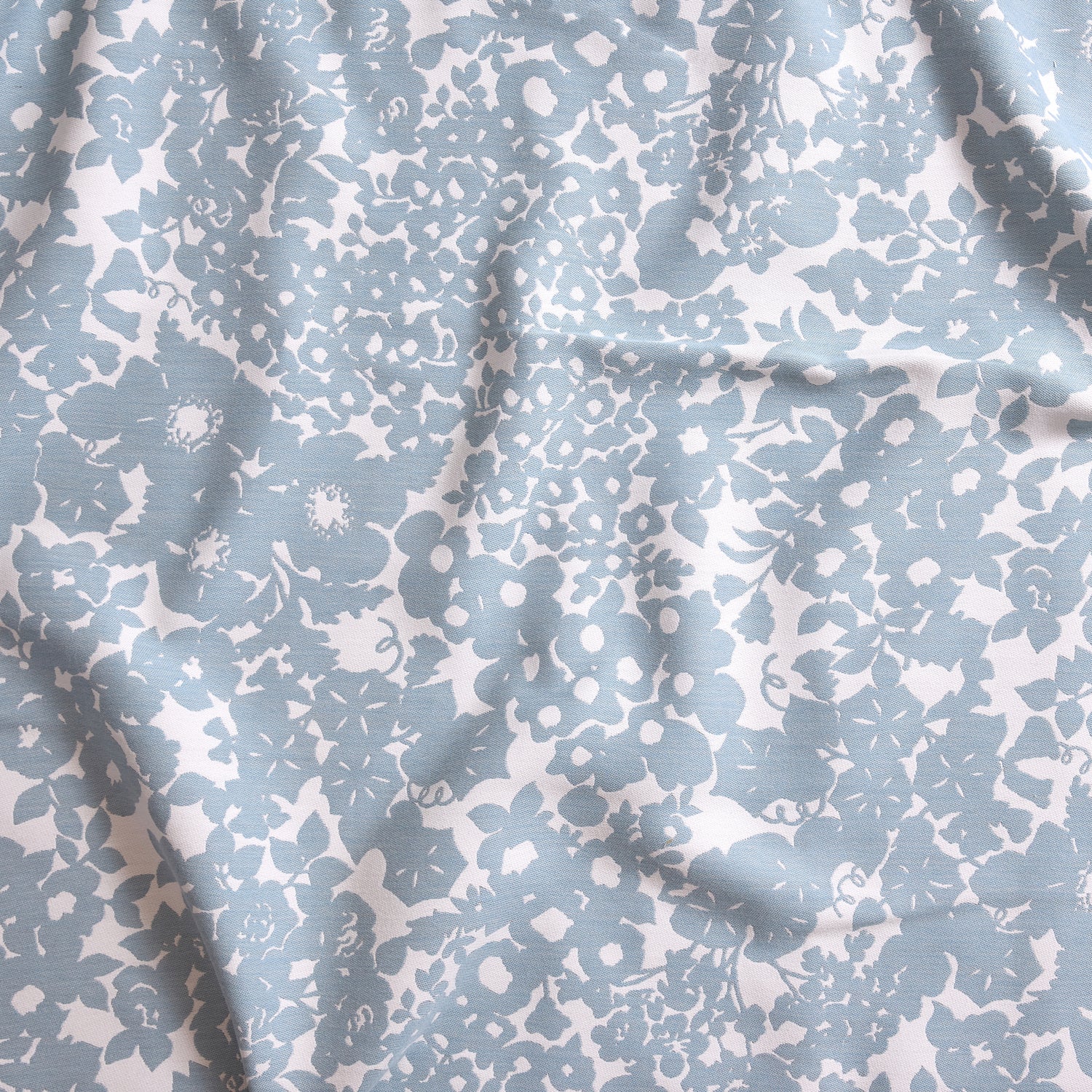 Close up of gently draped woven Indoor-Outdoor fabric with flower and leaf silhouette pattern in light blue on white background