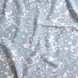 Close up of gently draped woven Indoor-Outdoor fabric with flower and leaf silhouette pattern in light blue on white background